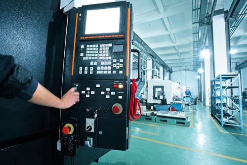 workers operating the controls of a CNC machine that manufactures parts for the aerospace Industry.
